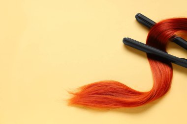 Soluk sarı arka planda kızıl saç teli ile saç düzleştirici.