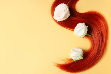 Kızıl saç teli ve soluk sarı arka planda çiçekler, yakın plan.