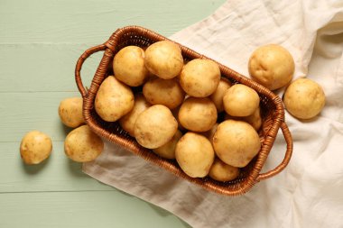 Yeşil ahşap arka planda çiğ patatesli hasır sepet