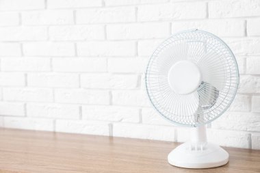 Beyaz tuğla duvarın yanındaki masada modern elektrikli vantilatör var.