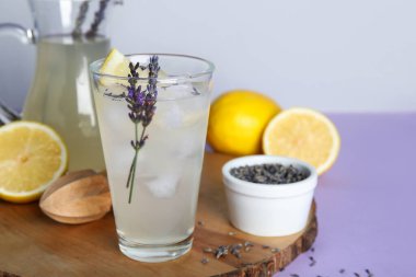 Ahşap tahta tahta, bir bardak soğuk lavantalı limonata, limonlar ve renkli masa üzerinde çiçekler.