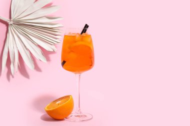 Bir bardak Aperol spreyli kokteyl ve pembe arka planda kağıttan yapılmış palmiye yaprağı.