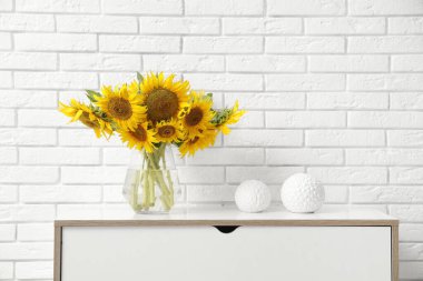 Beyaz tuğla duvarın yanındaki çekmecelerde ayçiçekli vazo.