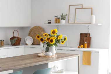 Ayçiçekli vazo, çaydanlık ve bardaklar açık mutfakta yemek masasında.