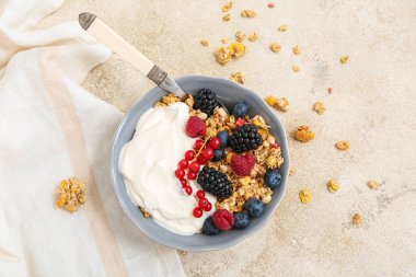 Bir kase lezzetli tahıllı yoğurt ve arkaplanda farklı meyveler.