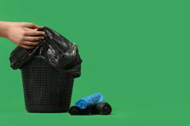 Yeşil arka plandaki çöp kutusundan çöp torbası alan kadın.