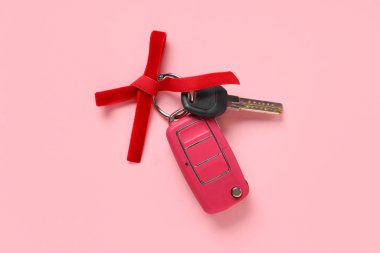 Pembe arka planda kırmızı fiyonklu yeni arabanın hediye anahtarları.