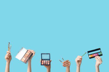 Farklı göz falı paletleri olan kadın elleri ve mavi arka planda makyaj fırçaları.