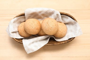 Tahta arka planda susam tohumlu bir tabak taze çörek.