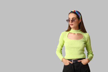 Şık güneş gözlüklü ve gri arka planda saç bandı takan güzel bir genç kadın.