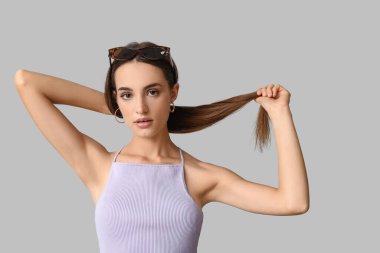 Gri arka planda şık güneş gözlüklü güzel bir genç kadın.