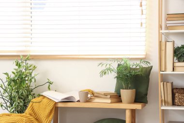 Kitaplık ve bankta kitaplar, bir fincan çay, ekose ve ev bitkileri oturma odasının içinde.