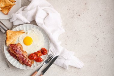 Beyaz arka planda kızarmış yumurta, pastırma, tost ve kurutulmuş domates tabağı. Üst görünüm