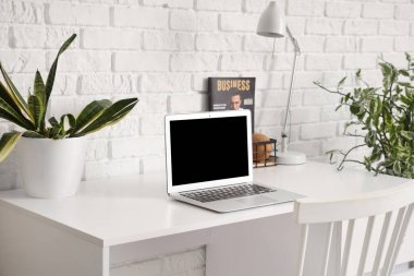 Laptop, lamba ve beyaz tuğla duvarın yanındaki ev bitkisinin olduğu modern masa.