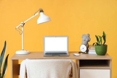 Sarı arka planda dizüstü bilgisayar, lamba ve bitki ile rahat