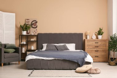 Yastıklı rahat bir yatak, raf ünitesi, çekmeceler ve şık bir yatak odasının içindeki koltuk.