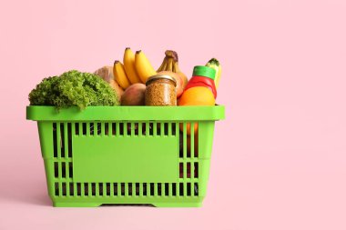 Farklı taze ürünlerle dolu yeşil alışveriş sepeti ve pembe arka planda hardal.