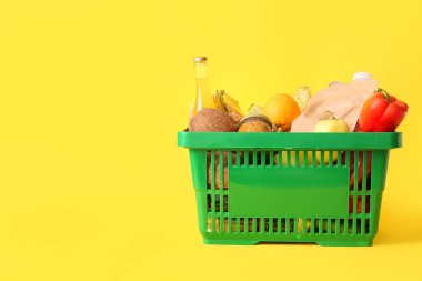 Farklı taze ürünlerle dolu yeşil alışveriş sepeti ve sarı arka planda dolma biber.