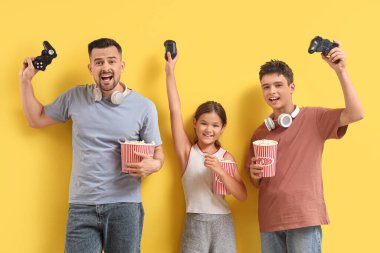 Baba ve çocukları sarı arka planda video oyunu oynuyorlar.