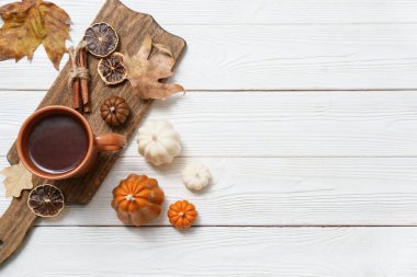 Balkabağı şeklinde mumlarla sonbahar kompozisyonu, bir fincan çay ve açık ahşap arka planda sonbahar yaprakları