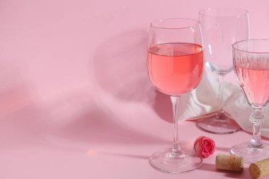 Şarap kadehleri, pembe arka planda gül ve bez.