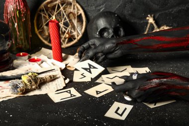 Yaşlı Futhark mühür kartlarıyla kanlı cadı elleri ve grunge siyah arka planda sihirli özellikler. Cadılar Bayramı