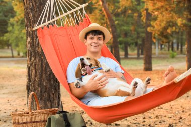 Beagle köpeği olan genç adam dışarıda kırmızı bir hamakta yatıyor.