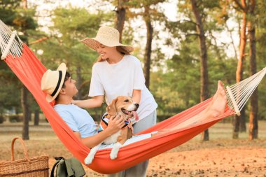 Beagle köpeği ve kız arkadaşıyla dışarıda hamakta dinlenen genç bir adam.