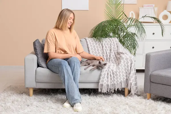 Evdeki kanepede oturan kedisi olan orta yaşlı bir kadın.