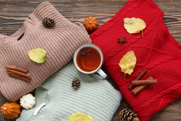 Şık kadın kazaklarıyla kompozisyon, bir fincan çay ve ahşap arka planda sonbahar dekoru.