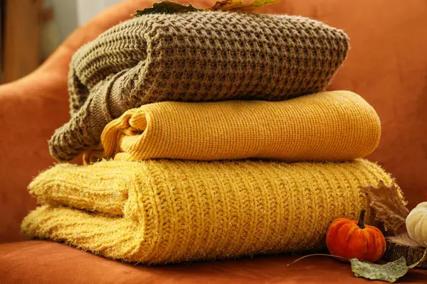 Turuncu koltukta sonbahar süslemeleri olan şık kıyafetler yığını oturma odasında, yakın plan.