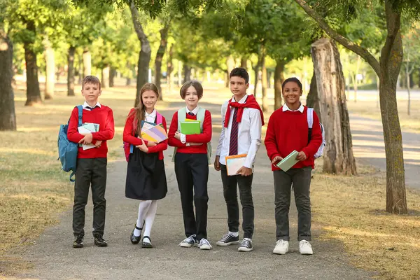 Kırtasiyeli bir grup mutlu öğrenci açık havada okula gidiyor.