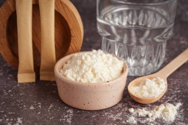 Bir bardak su, klozet, kolajen tozlu kaşık ve gri arkaplanda kese.