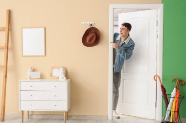 Genç adam koridorda açık bir kapıdan bir şeyi işaret ediyor.