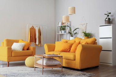 Oturma odasının içinde sarı kanepe, koltuk ve yeşil bitkiler var.