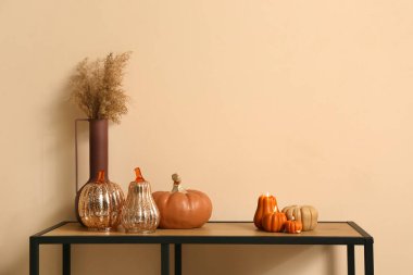 Evdeki bej duvarın yanındaki masada vazo ile balkabağı şeklinde mumlar yakıyor.