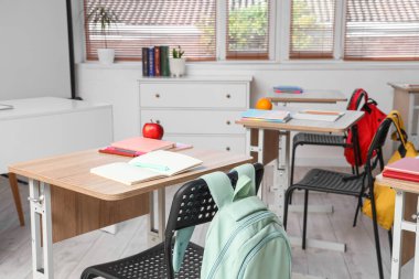 Boş sınıfta defterleri, elmaları ve kalemleri olan okul masası.