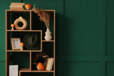 Yeşil duvarın yanında balkabağı, kitap ve dekor olan raf ünitesi.