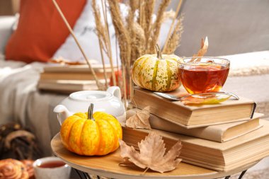 Bir fincan sıcak içecek, balkabağı, kitap ve sonbahar yapraklı bir çaydanlık.