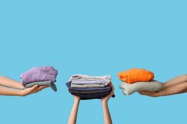 Mavi arka planda farklı giysi yığınları olan birçok kadın eli