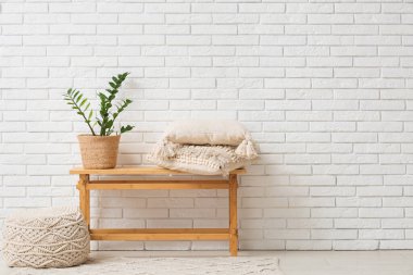 Yastıklı bank, ev bitkisi ve beyaz tuğla duvarın yanındaki oda.
