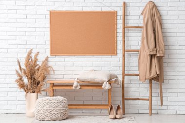 Benç, puf ve merdiven, oda beyaz tuğla duvarın yanında trençkot.