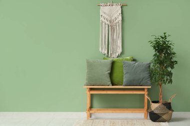 Dekoratif ağaç ve yeşil duvarın yanındaki minderli bankta.