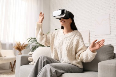Evdeki kanepede VR gözlük takan genç bir kadın.