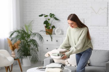 Genç bir kadın evdeki masaya kalın kazaklar koyuyor.