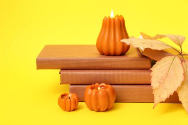 Kitap yığını, sonbahar yaprağı ve sarı arka planda yanan mumlar.