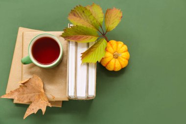 Yeşil arka planda kitap yığınları, balkabağı ve sonbahar yapraklarıyla kompozisyon
