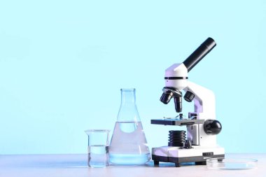 Modern mikroskop ve beyaz masanın üzerinde sıvı bulunan laboratuvar camları.