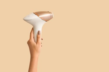 Bej arka planda modern fotoepilatörü olan kadın eli. Yasaklama kavramı