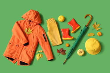 Yeşil arka planda şık çocuk kıyafetleri, aksesuarlar, balkabakları ve sonbahar yaprakları olan kompozisyon